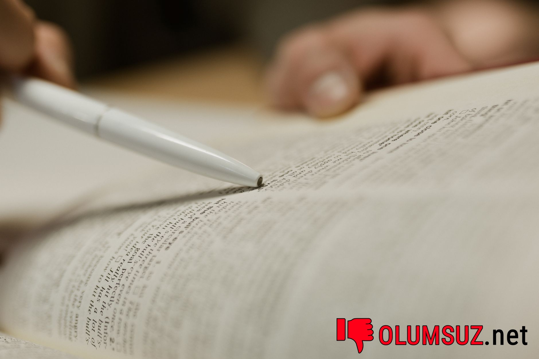 Masa üzerindeki kitap metnine işaret eden bir kalem yakın çekimi.